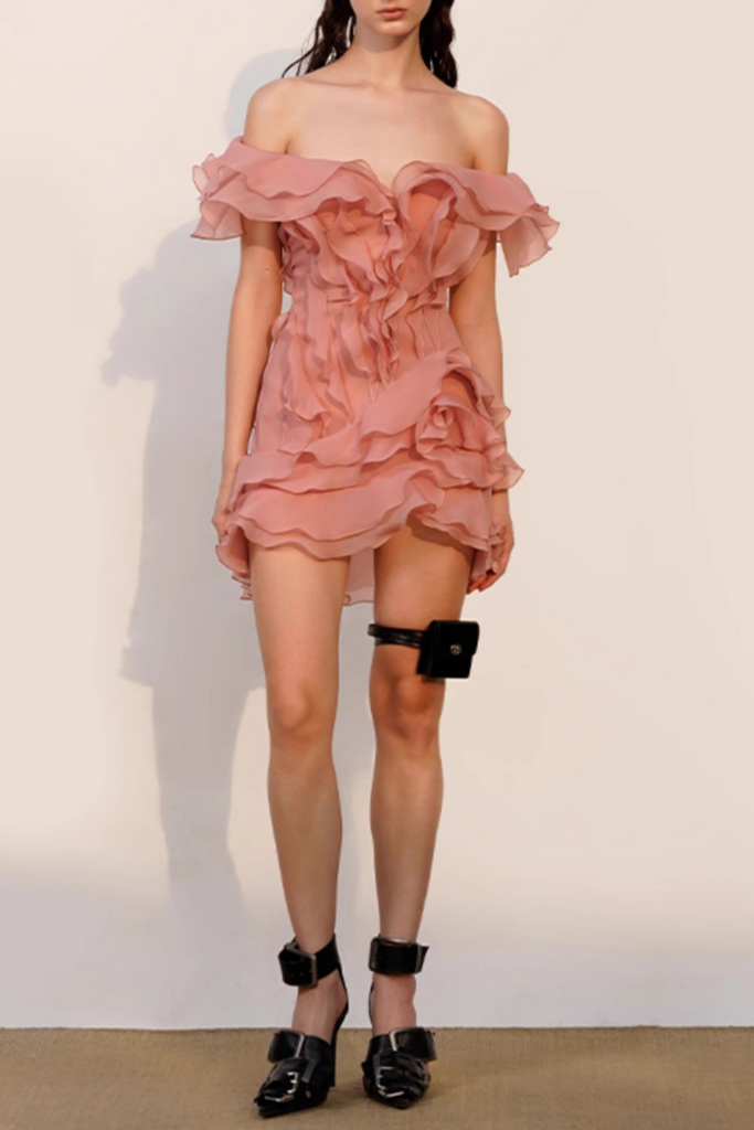 Woman wearing a pink ruffled dress with black shoes on a plain background