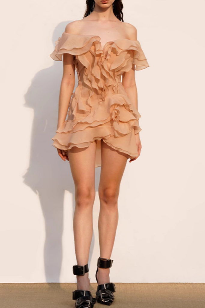 Woman wearing a beige off-shoulder ruffled dress against a plain background