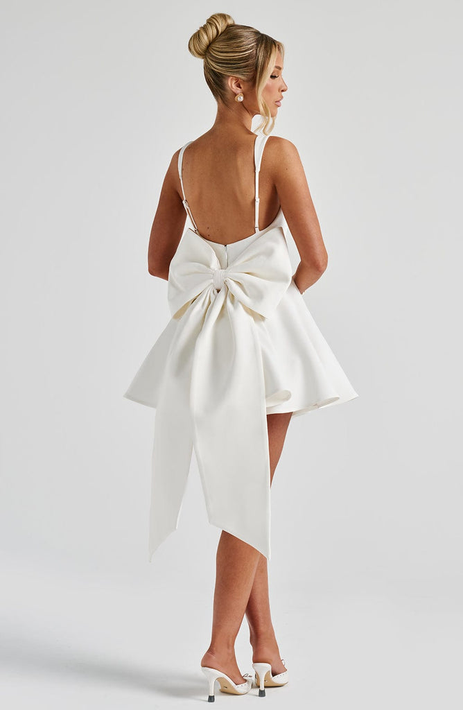 White dress with a large bow detail on the back, worn by a person on a plain background